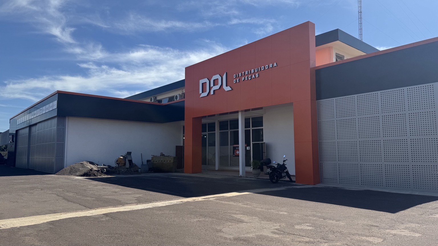 Fachada DPL Distribuidora de Peças — portal em ACM laranja com lettering aplicado e parede perfurada. Projeto MIDIAFIX.